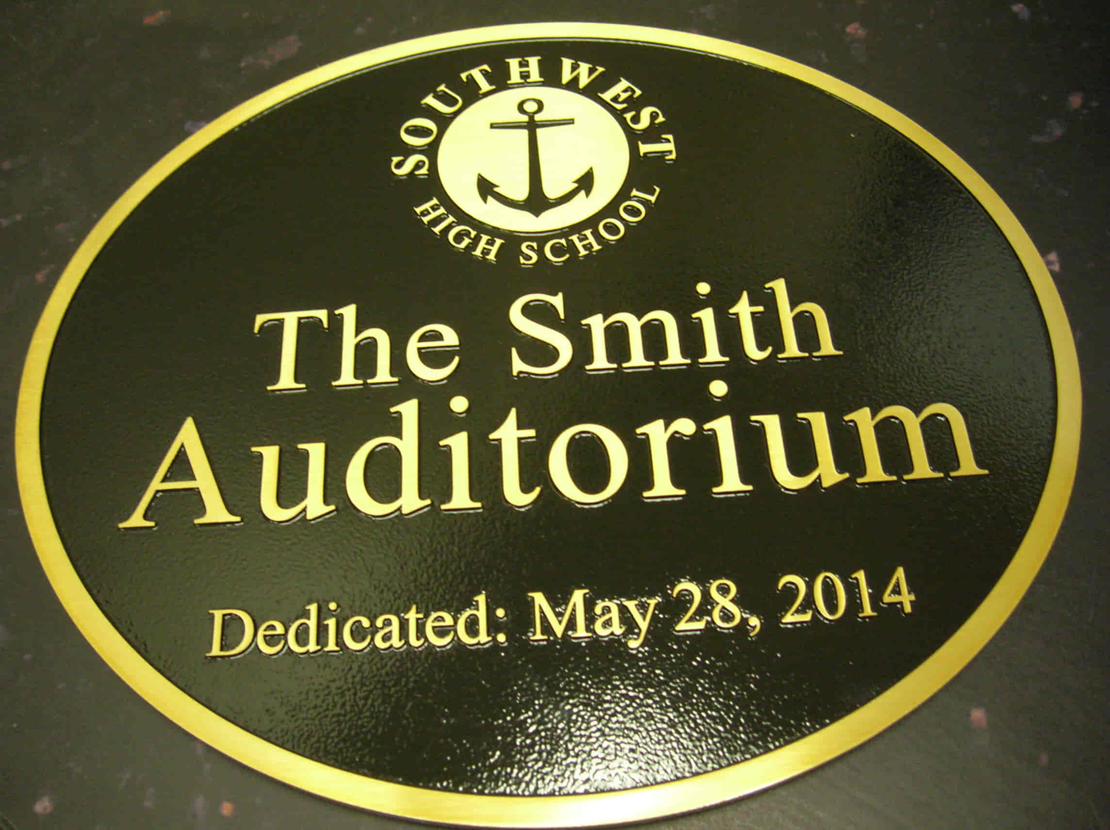 A brass dedication plaque for "The Smith Auditorium," featuring the Southwest High School logo and gold lettering on a black background.